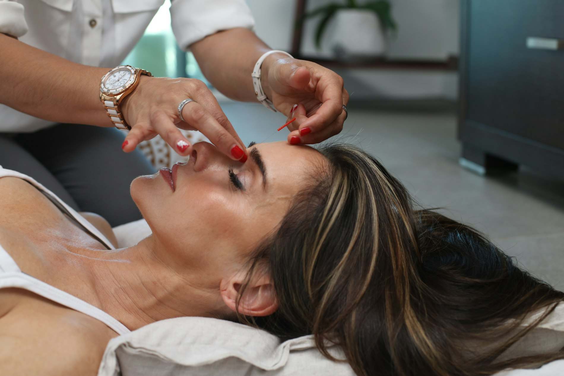 Mulher deitada de olhos fechados recebendo aplicação no rosto