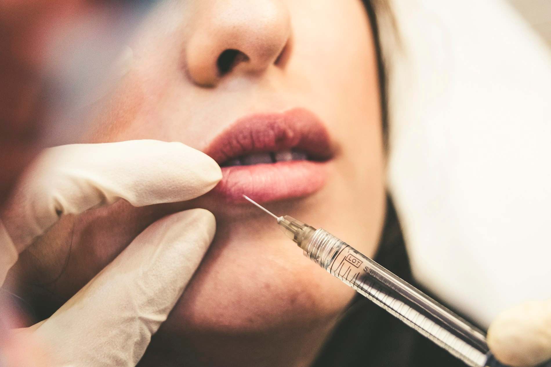 Mão de luva segurando seringa próxima aos lábios de uma mulher